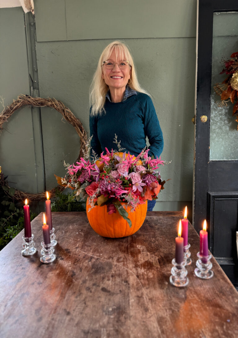 Great things to do in October header shot - April J Harris with a pumpkin floral centrepiece she made. There are candles on either side of the pumpkin.