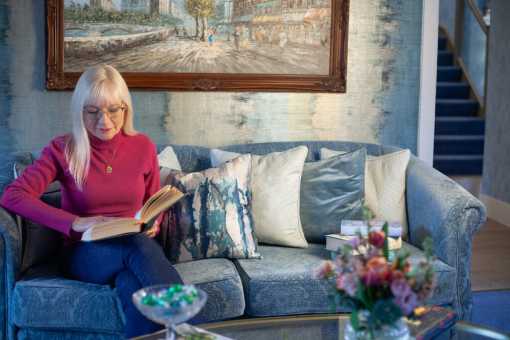 April Harris sitting on the sofa in her living room reading a book from her 25 Best Summer Reads book list
