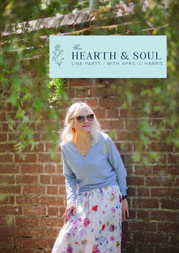 Header image for the last edition of Hearth and Soul April J Harris wearing a flowered skirt and blue cashmere jumper leaning against a brick wall with leaves trailing down it. Photo by Terry Joshi for April J Harris