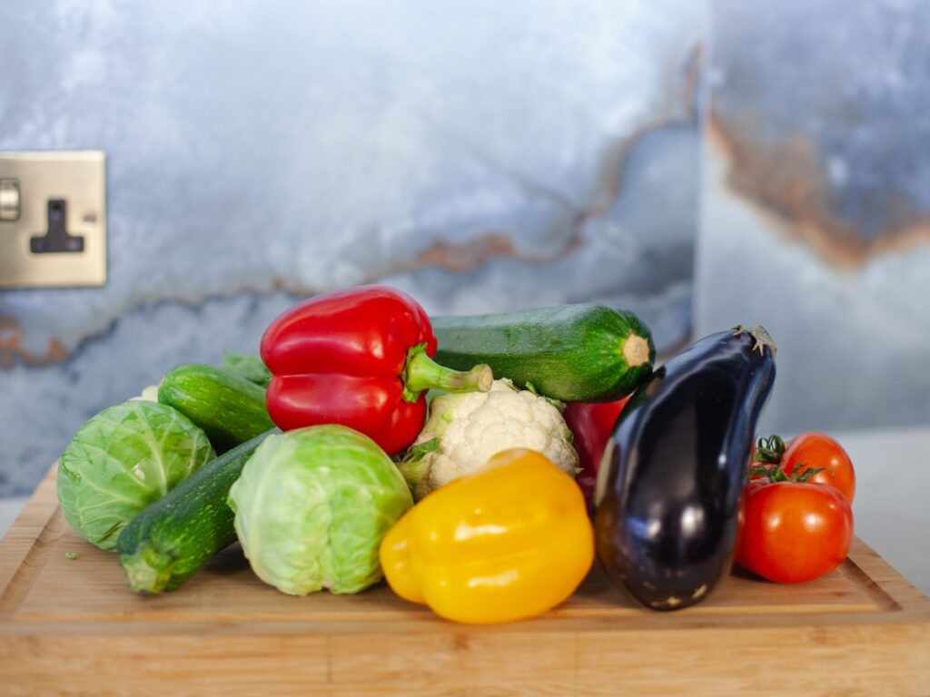 An assortment of colourful vegetables including red and yellow peppers, tomatoes and aubergine, sitting on a bread board.