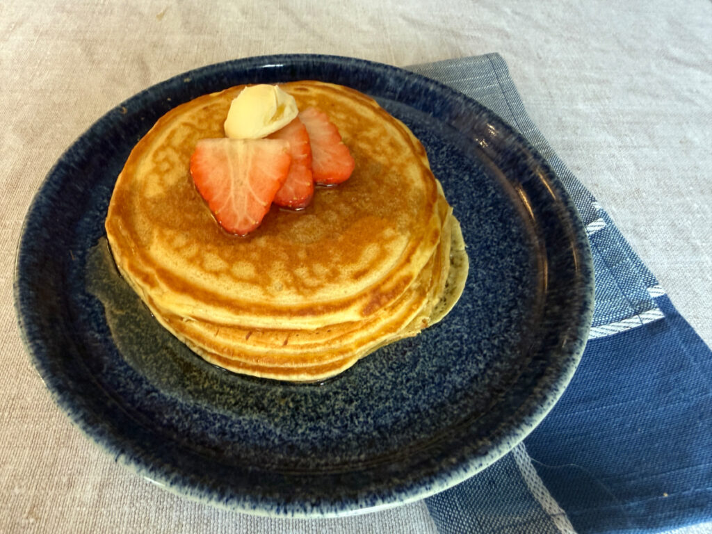 A stack of fluffy, dairy-free pancakes on a blue plate topped with dairy-free butter and strawberry slices