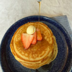 A stack of fluffy, dairy-free pancakes with syrup being poured o ver from a pitcher