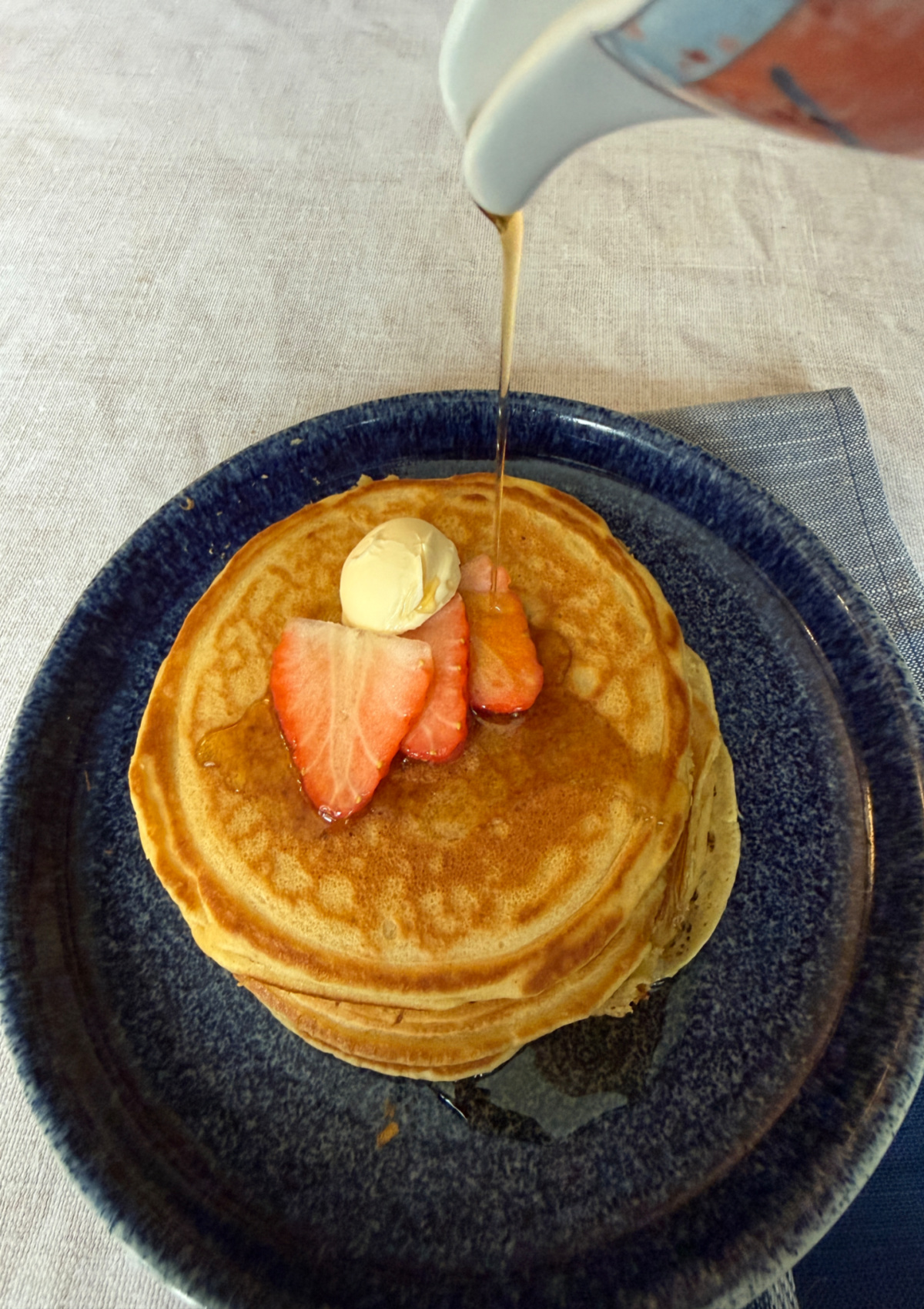 A stack of fluffy, dairy-free pancakes with syrup being poured o ver from a pitcher