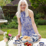 April Harris placing a tray with Apricot and Ginger Scones, clotted cream, apricot jam and a Blue Willow teapot on a table.