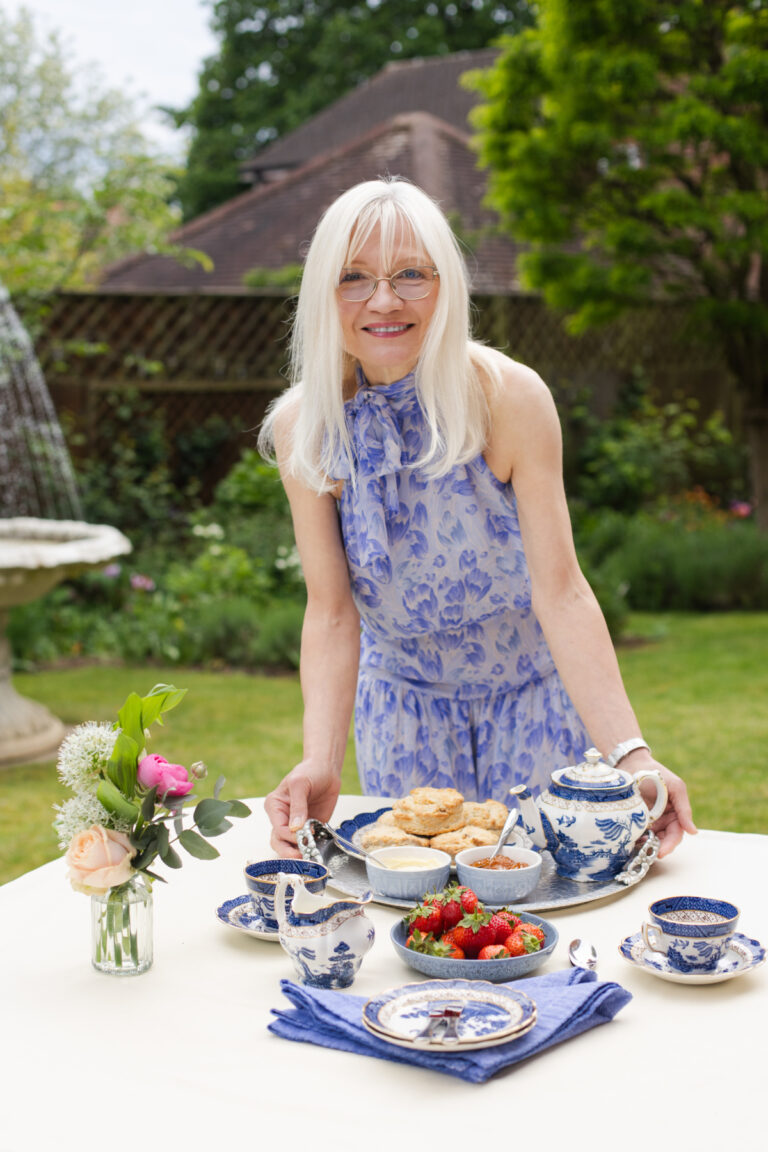 April Harris placing a tray with Apricot and Ginger Scones, clotted cream, apricot jam and a Blue Willow teapot on a table.